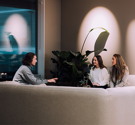 Foto av tre ansatte i Kvass som sitter i en sofa og prater