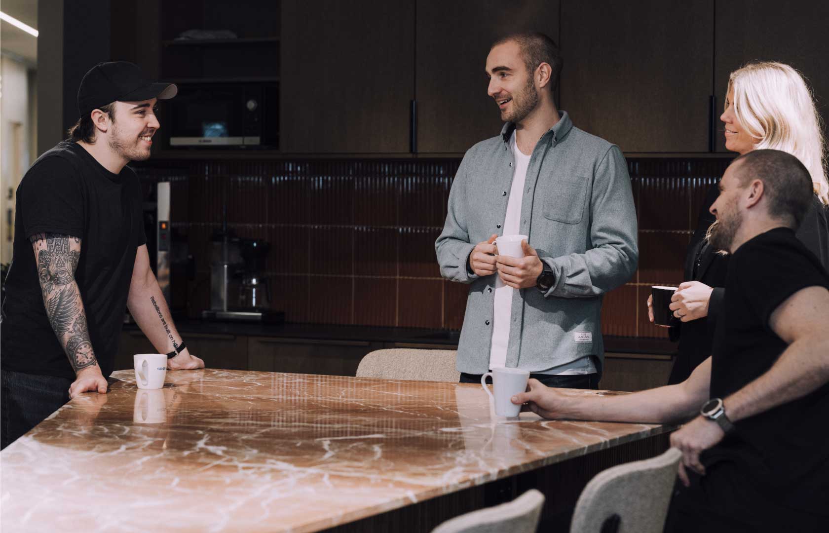 Fire ansatte i kvass samlet rundt et kaffebord i fellesarealet og prater